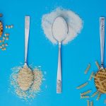 Four spoons with popcorn, rice, sugar, and pasta on a blue background. Perfect for food-related projects.
