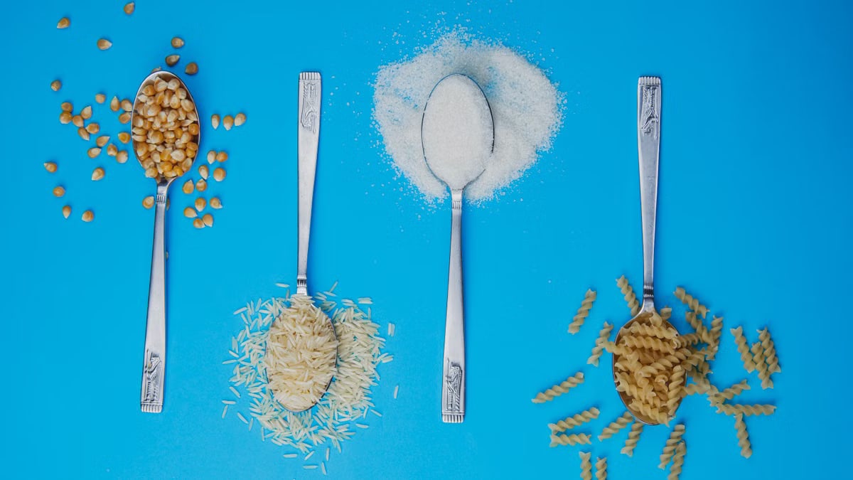 Four spoons with popcorn, rice, sugar, and pasta on a blue background. Perfect for food-related projects.